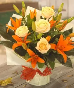 Autumn-themed flower arrangement featuring warm orange lilies and soft peach roses, beautifully presented in an aqua pack