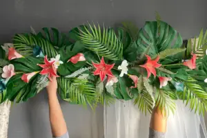 ft beach wedding archway decorated with tropical teal and coral flowers, palm and monstera leaves, and a corner swag garland, creating a vibrant coastal wedding backdrop