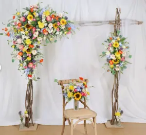 “Boho-style wildflower wedding arch decorated with sunflowers, daisies, dahlias, and ranunculus, perfect for a spring wedding backdrop, arbour, or gazebo