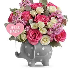 Adorable one-sided baby girl floral arrangement in a ceramic polka dot elephant container, featuring pink roses, white spray roses, pink stock, and dusty miller